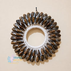 A circular seashell wreath wall hanging with a white braided rope center, photographed against a plain beige wall. A small black hook is attached at the top, and a Tropfe Artisan Klu watermark appears in the lower-left corner.