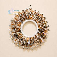 A circular shell wall hanging wreath made of numerous small seashell fragments arranged around a white rope center, shown against a plain beige background. A Tropea Artisan logo is visible in the upper left.