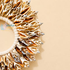 A close-up of a decorative wreath made from natural seashells and white rope, arranged on the left side of a warm beige background. The shells show natural tan, cream, and brown tones with some silver-gray highlights.
