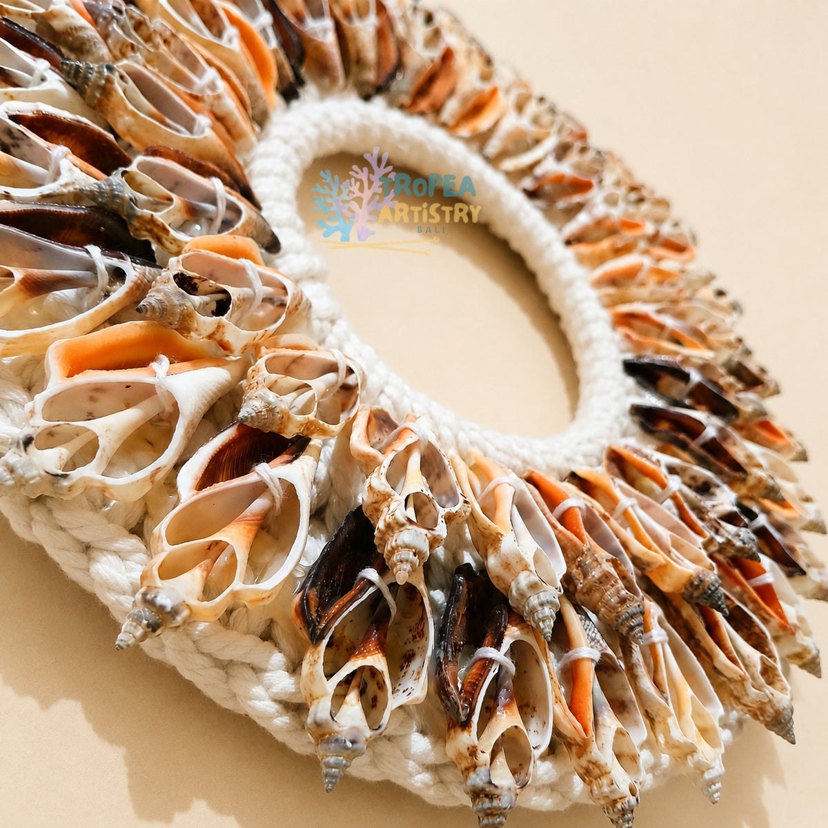 A handmade circular bag or wreath made from numerous natural seashells arranged around a thick white rope base, photographed on a plain beige background. A semi-transparent 'ROPEA ARTistry' watermark is visible in the center.