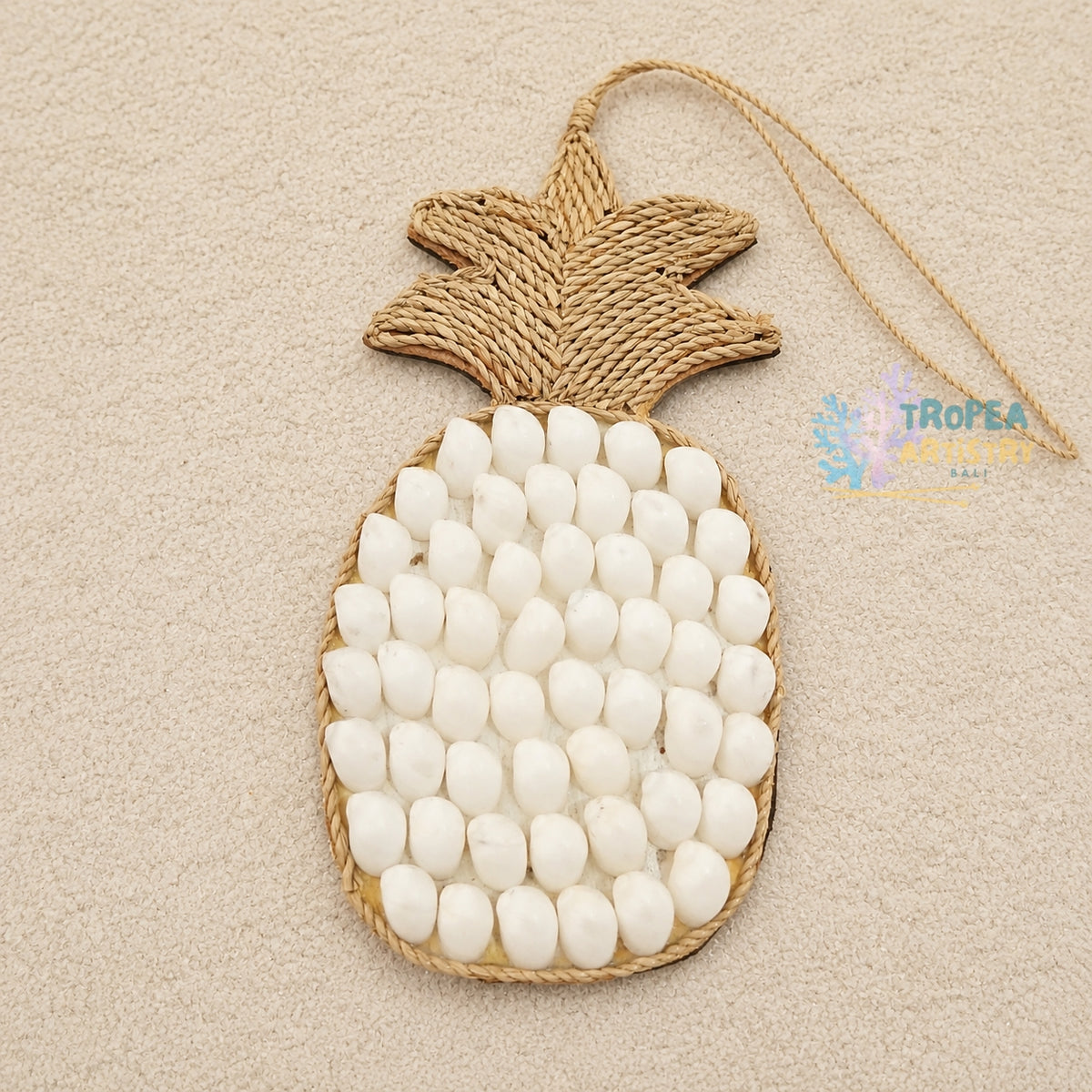 A pineapple-shaped wall hanging or ornament made from natural jute rope and white oval stones, photographed on a light beige textured background.