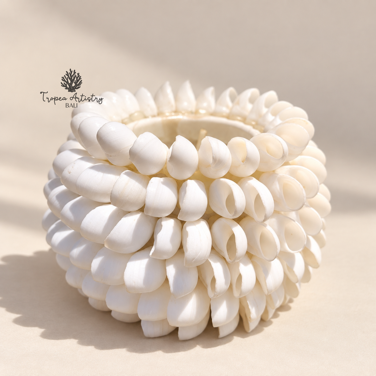 A white sculptural ceramic pot or planter with a textured, layered petal-like design, photographed on a warm beige background with soft shadows. A watermark logo for 'Trapeen Orchid Bag' is visible in the upper left.