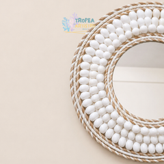 A close-up of a round decorative mirror with a white beaded border and natural rope trim, photographed on a warm beige background. A Tropea Artists Bali watermark is visible near the top center.