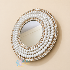 Round decorative wall mirror with a thick white rope border and rows of white pebble-like accents, shown against a warm beige wall.