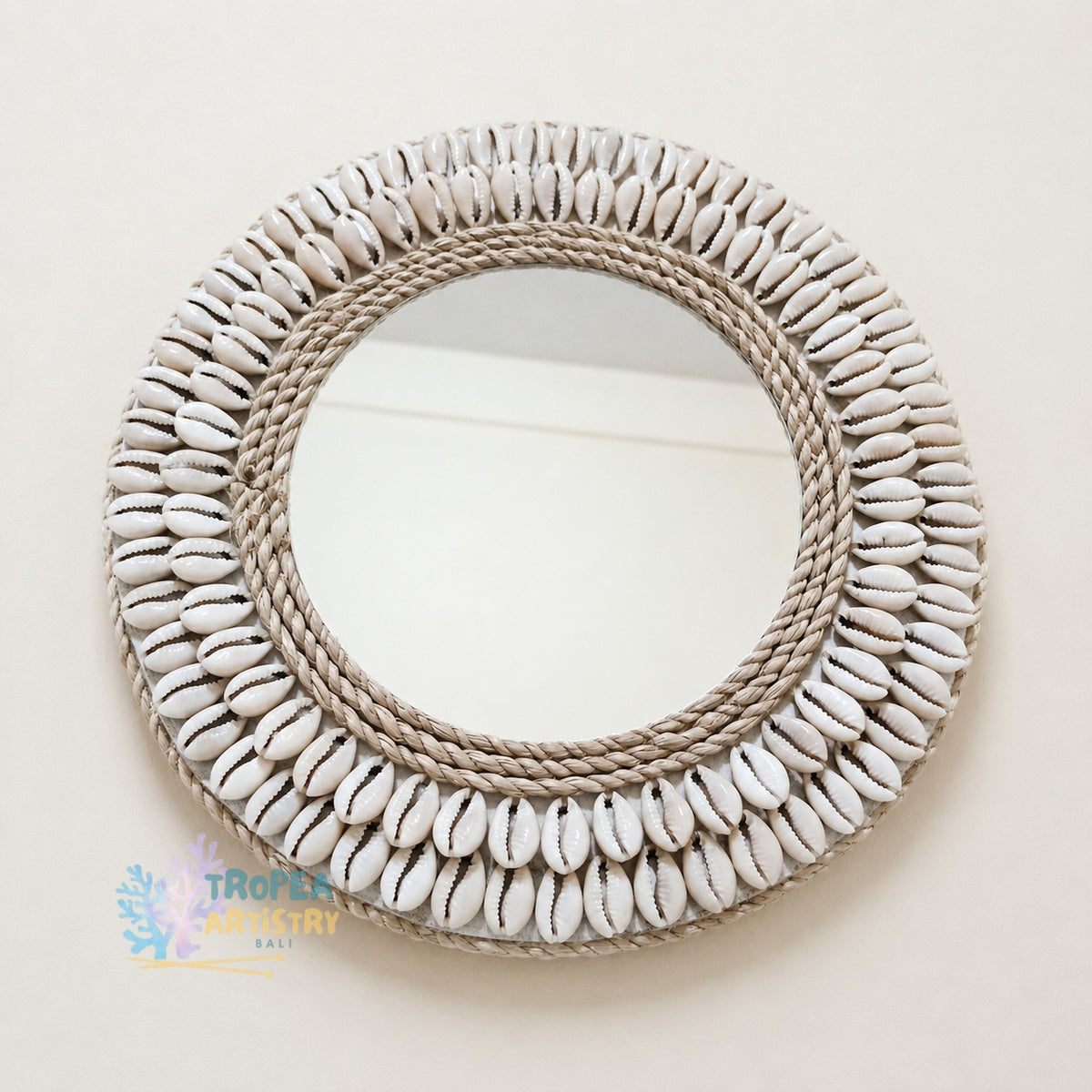 A round decorative wall mirror with a thick rope border and multiple concentric rings of white cowrie shells, shown against a plain off-white background.