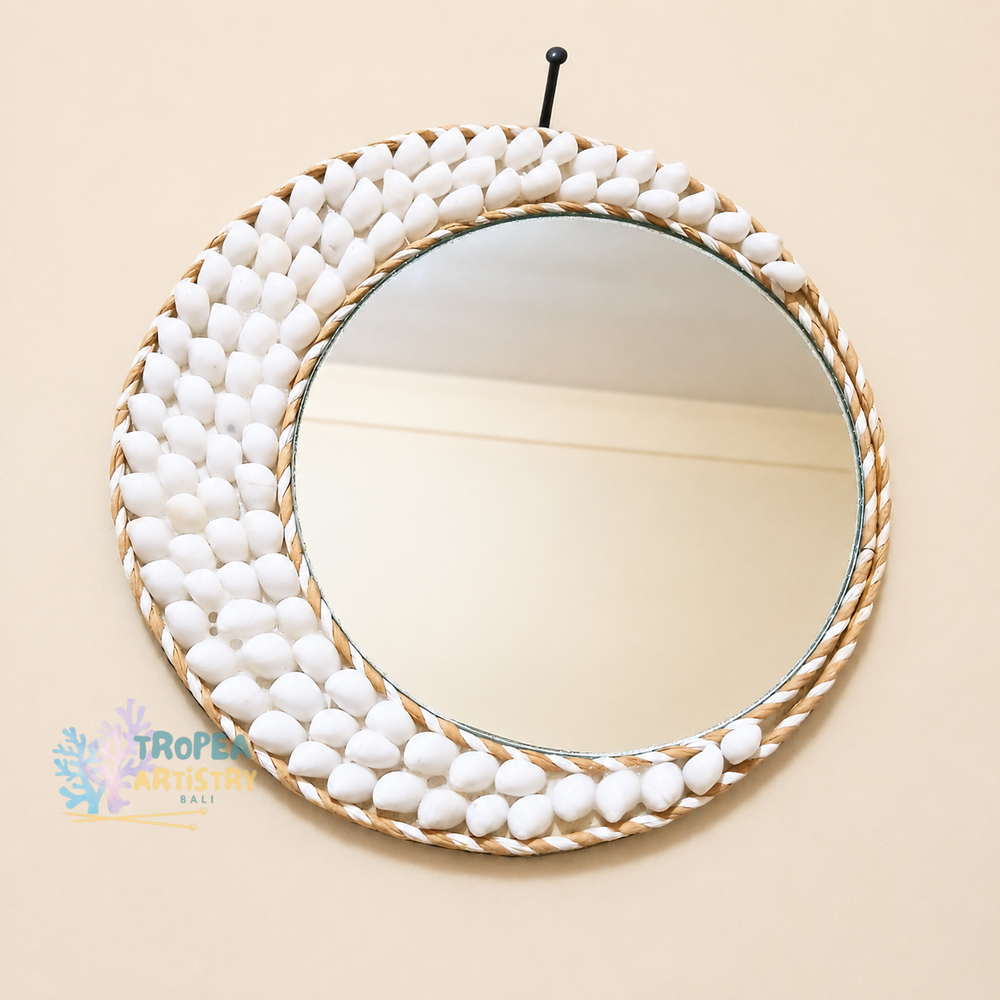 Round wall mirror with a decorative border made of small white pebbles and a twisted rope edge, hanging on a beige wall.