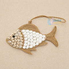 A decorative fish-shaped wall hanging or ornament made from natural rope and white and beige shells, photographed on a light beige textured background. A small black bead eye and a hanging loop are visible.