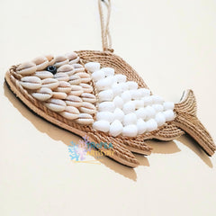 A decorative fish-shaped wall hanging made from woven natural rope and shell-like pieces, with a small black bead for an eye, shown on a plain light beige background.