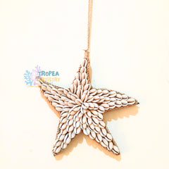 A starfish-shaped hanging ornament made from small white seashells and wrapped in natural twine, suspended by a twine string against a plain cream background.