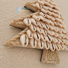 A triangular wooden wall decor piece covered with rows of beige cowrie shells, photographed on a textured beige fabric background.