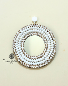 A round decorative mirror with a thick, multi-layered border of white beads and brown-and-white braided rope, hanging on a light beige wall.