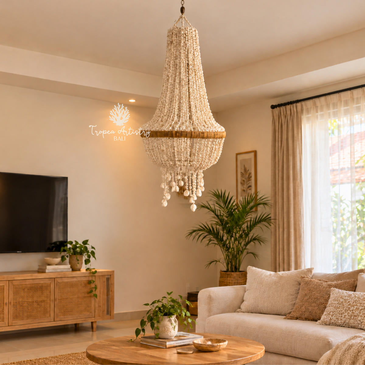 A large, elegant beaded chandelier with a gold band and crystal-like hanging drops, suspended in a bright, modern living room with a beige sofa, wooden TV stand, and potted plants.